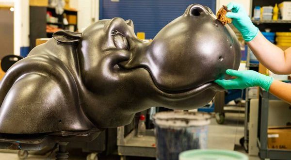 A guest offers a treat to a lifelike hippo sculpture in a whimsical workshop, echoing the magic of Disney's Riviera Resort.