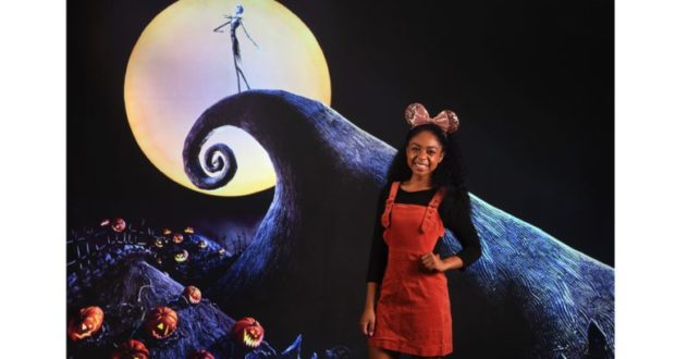 Capture Halloween memories at Disney Springs with a guest in mouse ears before the iconic Nightmare Before Christmas backdrop.