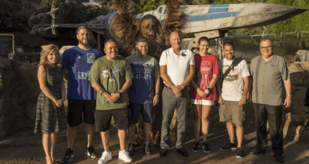 Fans gather for a photo with Chewbacca and an X-wing at Star Wars: Galaxy's Edge, enjoying the sunny park atmosphere.