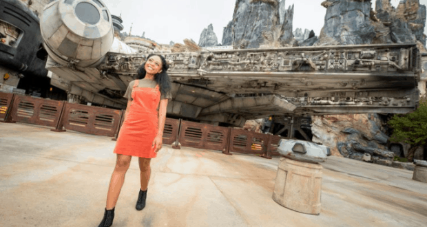 A guest in an orange dress beams in front of the Millennium Falcon at Star Wars: Galaxy’s Edge, capturing that iconic Disney shot.