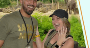 Happy couple in matching safari shirts at Animal Kingdom, her ring sparkling after a magical Disney proposal with elephants nearby.