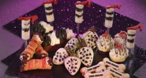 Cruella-inspired Halloween desserts at Disney World: bone-shaped cookies and white chocolate-dipped treats on a festive platter.