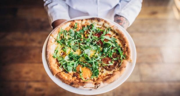A guest at Disney Springs showcases a colorful, veggie-packed pizza topped with arugula—pure culinary magic in every bite.