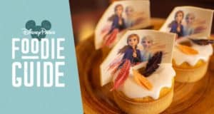 Frozen 2-themed cupcakes with character toppers and feathers displayed beside the Walt Disney World Foodie Guide sign.