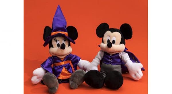 Mickey Mouse and Minnie Mouse plush toys dressed in Halloween costumes pop against an orange backdrop, celebrating Disney Parks fun.