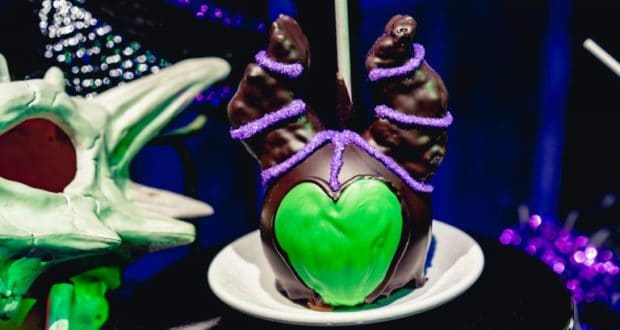 Maleficent candy apple with chocolate horns and purple glitter on a white plate, just like at Disneyland’s magical treat spots.