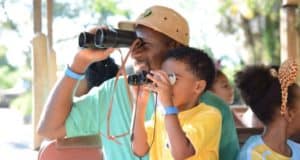 Guests and kids at Disney’s Animal Kingdom smile and use binoculars, joining the Protect the Pride lion conservation efforts.