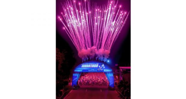 Fireworks dazzle above runners at the Walt Disney World marathon start, with a glowing blue arch setting the magical scene.