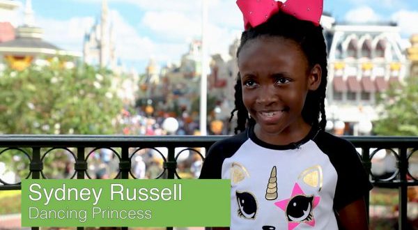 Sydney Russell, Dancing Princess, beams in a unicorn tee and pink bow outside at Walt Disney World.