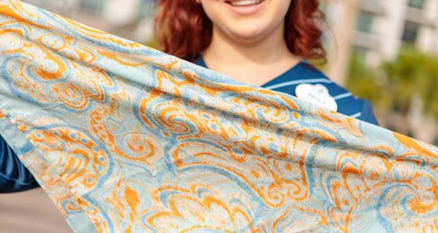 A guest shows off a vibrant blue and orange paisley scarf outdoors, channeling the bold style of Disney Cast Costumes.