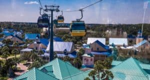 Disney Skyliner gondolas soar over Caribbean Beach Resort, gliding past palm trees on a bright day at Walt Disney World.