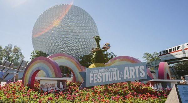 Epcot Festival of the Arts sign surrounded by vibrant flowers and rainbow arches, with Spaceship Earth as the iconic backdrop, 2020.
