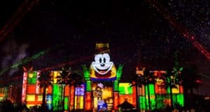 Mickey Mouse and festive patterns light up a Disney World building as lasers and stars dazzle the night at Jingle Bell Jingle BAM.