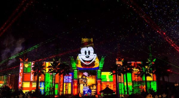 Mickey Mouse and festive patterns light up a Disney World building as lasers and stars dazzle the night at Jingle Bell Jingle BAM.