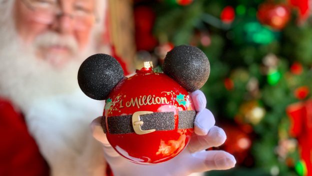 Santa celebrates 1 million guests, holding a red Mickey ornament in front of a glittering tree on Disney Springs’ Tree Trail.