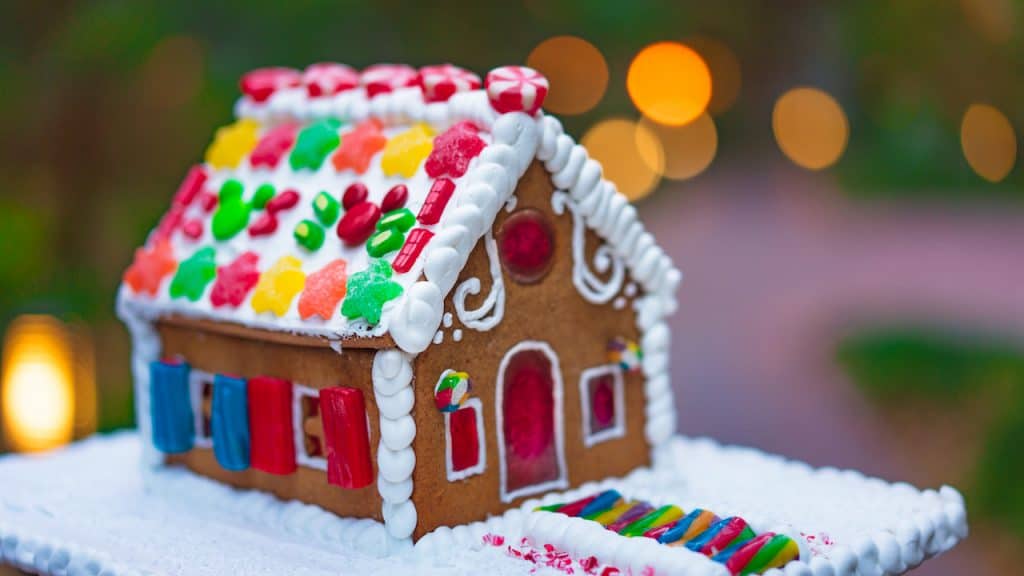 A Disney Parks-inspired gingerbread house decked with candies and icing sits on snowy white, capturing festive holiday magic.