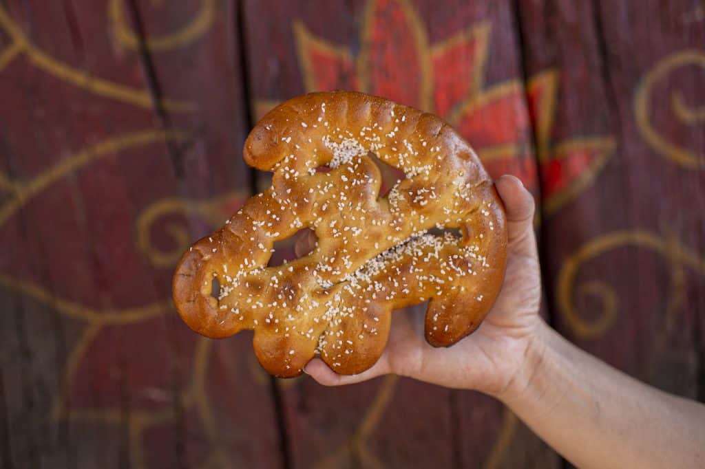 Sesame-topped, elephant-shaped Disney Parks bread held up against a decorative wooden wall, as seen in Best Bites Dec 2019.