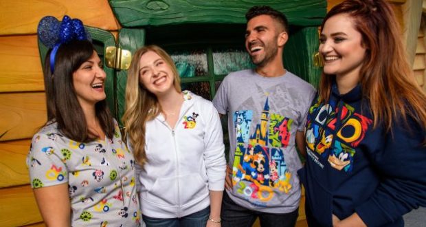 A group of friends in Disney Parks apparel laugh together outside Mickey’s Toontown house, surrounded by vibrant colors.