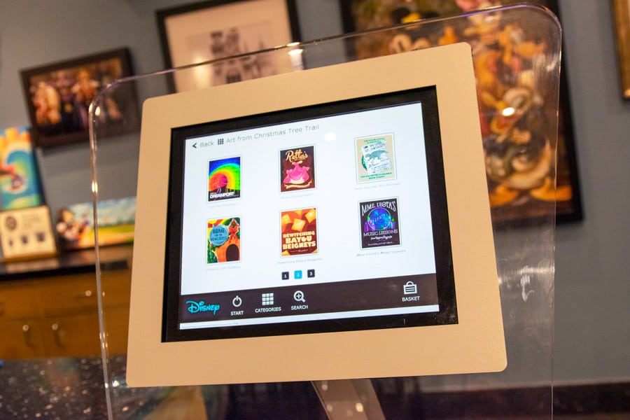 A digital display in the gallery features Disney art prints, framed by festive decor reminiscent of the Disney Springs Tree Trail.