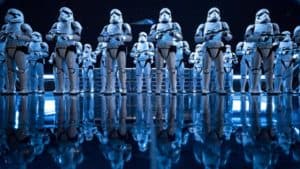 Stormtroopers in gleaming white armor line up under blue lights, reflected on the glossy floor inside Star Wars: Rise of the Resistance.