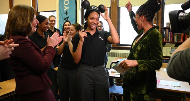 A Disney Dreamers Academy student beams in Mickey Mouse ears while classmates cheer her on, radiating magical Disney spirit.
