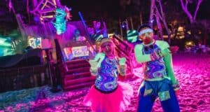 Guests in neon outfits dance on the glowing beach at Typhoon Lagoon’s H2O Glow Nights, surrounded by festive Disney decor.