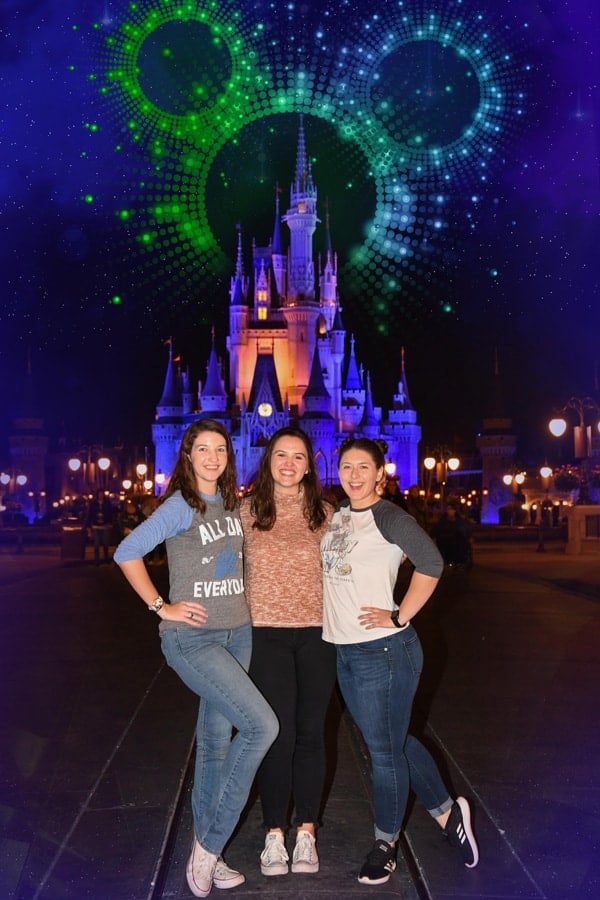 Friends smile in front of Cinderella Castle as fireworks burst overhead, enjoying a Disney PhotoPass night at Magic Kingdom.