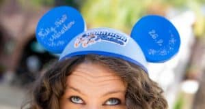 Disney fan beams in blue Mickey Mouse ears reading "Marathon Finisher" and "My First Marathon," celebrating runDisney victory.