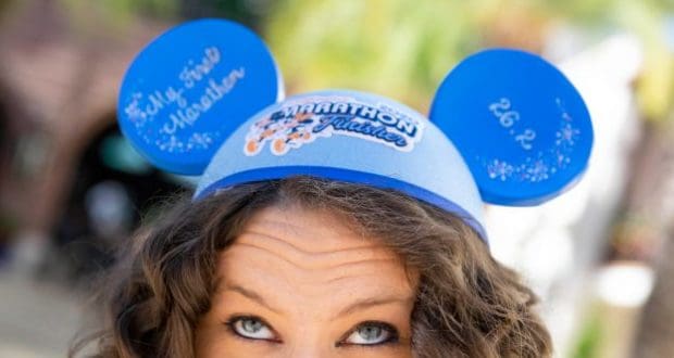 Disney fan beams in blue Mickey Mouse ears reading "Marathon Finisher" and "My First Marathon," celebrating runDisney victory.