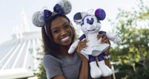 Disney fan sporting Minnie Mouse ears poses with a Minnie plush in front of Space Mountain at Magic Kingdom.
