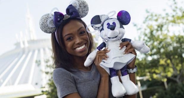 Disney fan sporting Minnie Mouse ears poses with a Minnie plush in front of Space Mountain at Magic Kingdom.