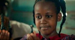 A young girl inspired by Disney’s Queen of Katwe gazes thoughtfully at a chess piece, ready for her next magical move.