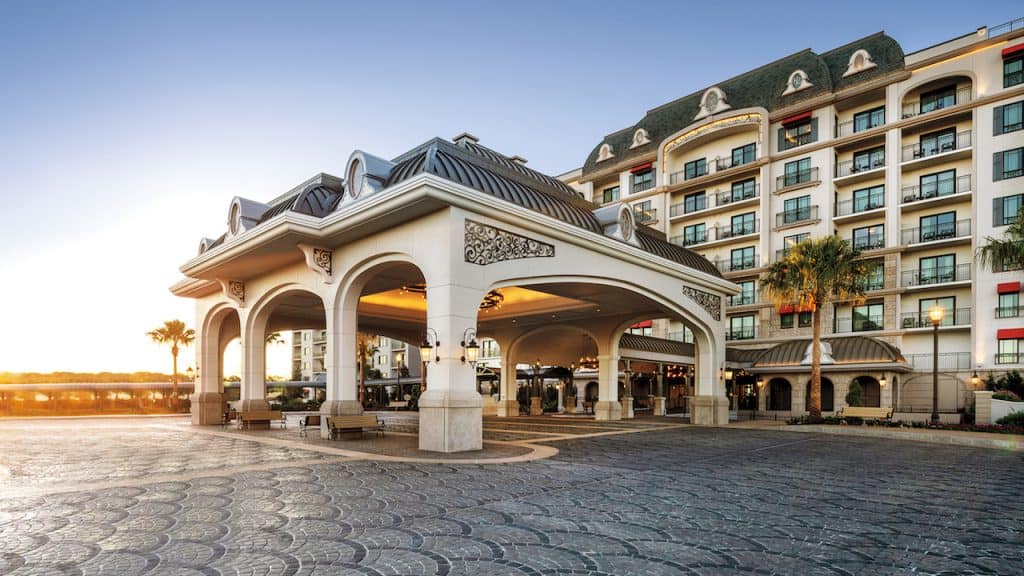 Grand Disney-area hotel entrance with soaring arches and magical details, multi-story building glowing at sunset near the theme parks.