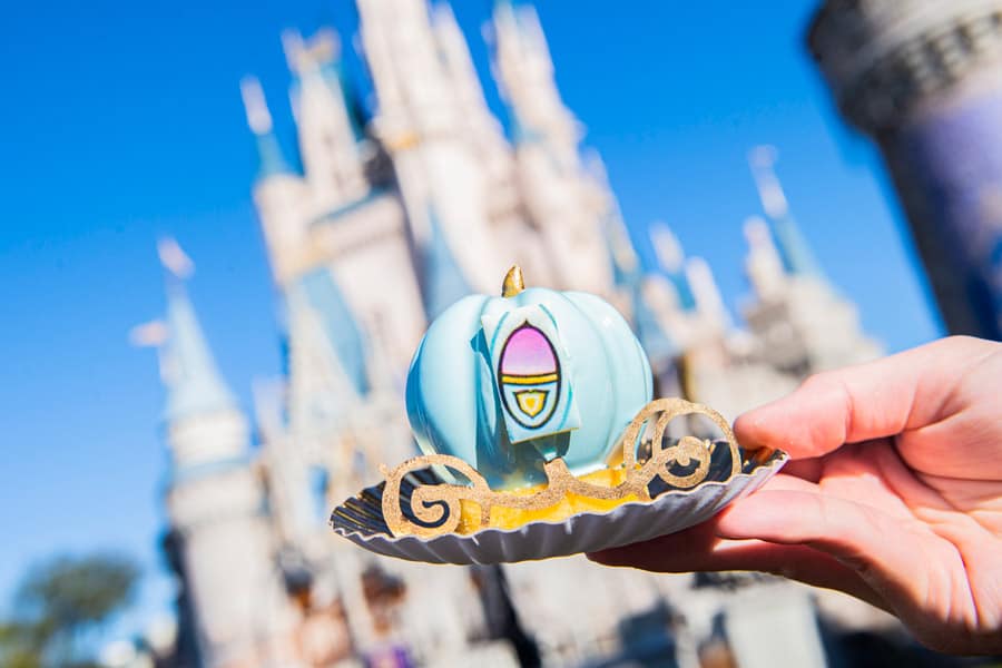 Cinderella-inspired dessert held up before the iconic Disney castle, shining beneath clear blue skies at Walt Disney World.
