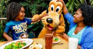 A family beams as they greet Pluto at their Walt Disney World Resort restaurant, savoring food, drinks, and magical Disney fun.