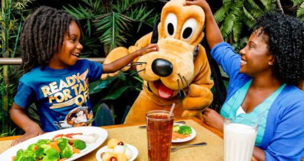 A family beams as they greet Pluto at their Walt Disney World Resort restaurant, savoring food, drinks, and magical Disney fun.