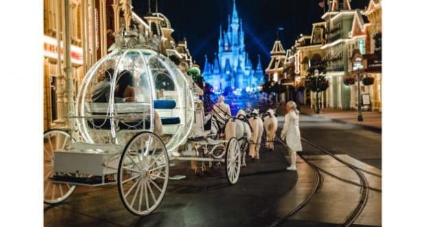 A sparkling Cinderella carriage glides past the castle at night, drawn by white horses along Main Street in Walt Disney World.