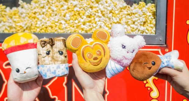 Wishables plushes—popcorn, churros, Mickey Mouse, bunny, turkey leg—held at Disney Parks with popcorn piles in the background.