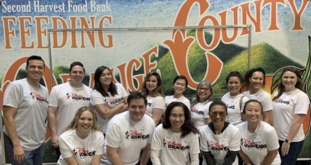 Disneyland Resort volunteers in matching shirts smile by a "Feeding Orange County" food bank sign, celebrating their charitable success.