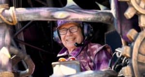 Festival of Fantasy Parade performer in vibrant purple costume and headset operates whimsical gears, bringing parade magic to life.