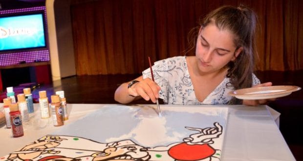 A guest channels Disney Cruise Line magic, painting a vibrant Disney-themed masterpiece at a table surrounded by colorful paints.