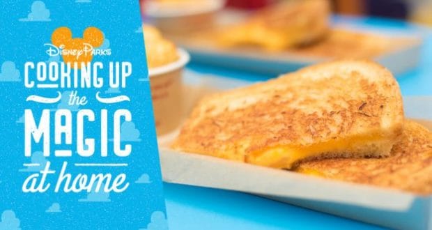 Toy Story Land grilled cheese sandwiches on trays by a blue Disney Parks sign, celebrating National Grilled Cheese Day.