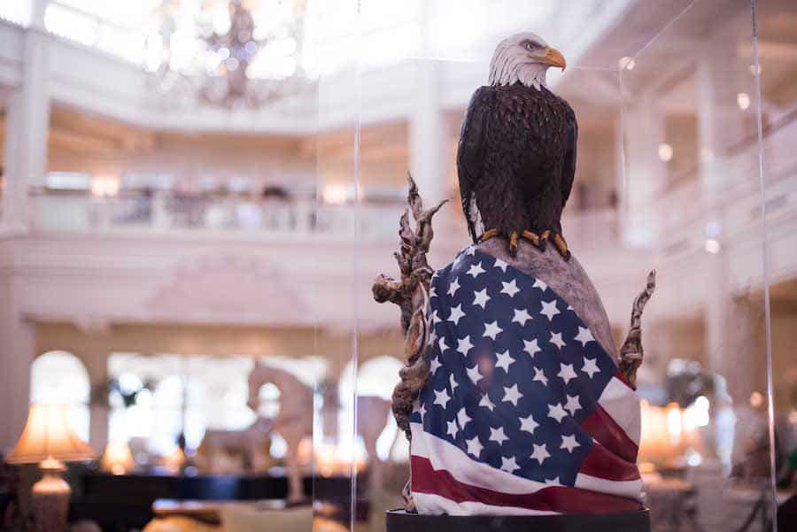 A majestic bald eagle statue with an American flag at its base gleams in a bright Disney World room, part of the Easter Egg Displays.