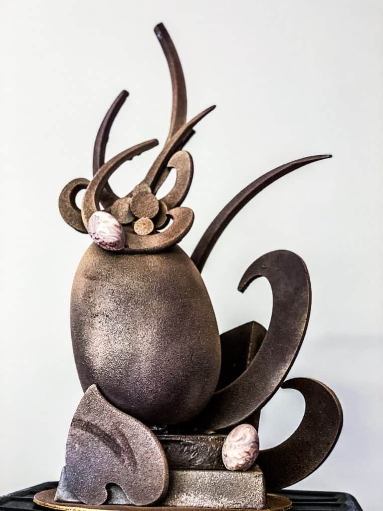 Whimsical chocolate sculpture with flowing curves and marbled eggs, channeling the playful spirit of Disney World’s Easter egg displays.