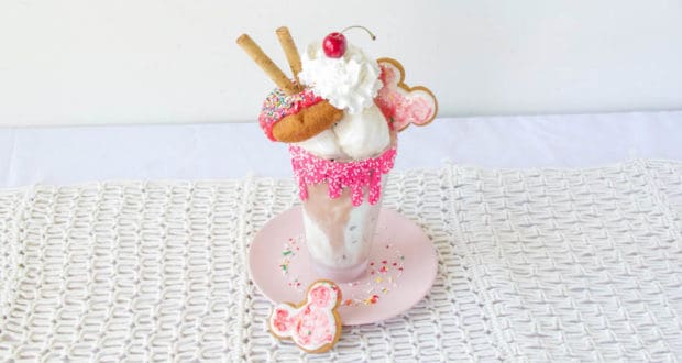 Ultimate Sundae-style vanilla milkshake in a pink glass, topped with whipped cream, candy, and cookies—just like at Disney Parks.