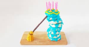 Blue-frosted cakes with candles and a yellow broomstick, styled like Disneyland’s whimsical Sleeping Beauty Donut Cake, on wood.