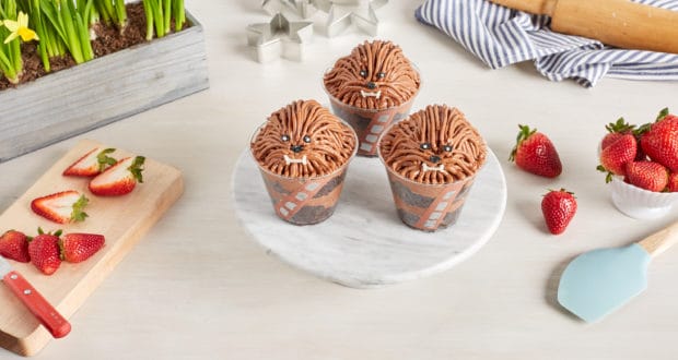 Chewie Cake Cups, inspired by Star Wars, are displayed on a stand with strawberries and baking tools—a Galaxy’s Edge treat for fans.