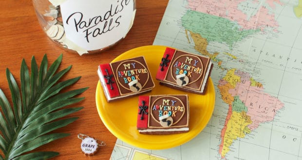 Up-themed "My Adventure Book" cookies on a yellow plate, next to a Paradise Falls jar and map—perfect for Pixar fans on adventure!.