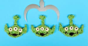 Green alien Rice Crispy Treats under a silver claw on Toy Story Land-inspired blue, evoking the iconic Pixar attraction.