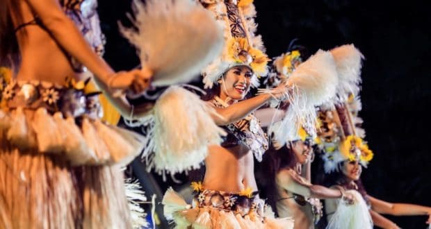 Aulani Resort hosts National Lū‘au Month with performers in vibrant Polynesian attire, feather headdresses, and festive fans.